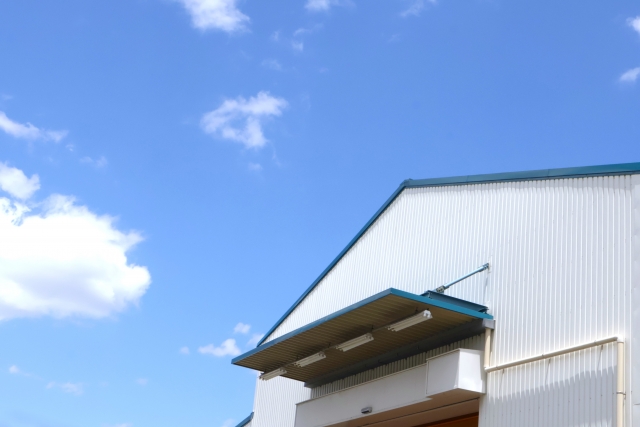 青空の下に建つ工場の外観(白い外壁と屋根が特徴的な建物)